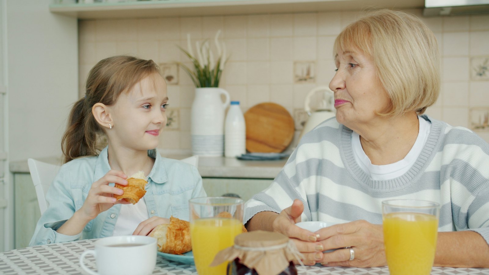 A grandmother and granddaughter share breakfast at the kitchen table.